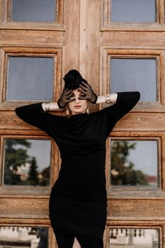 Stylish woman in the city. Fashion photo of a beautiful model in an elegant black dress posing against the backdrop of a building on a city street.