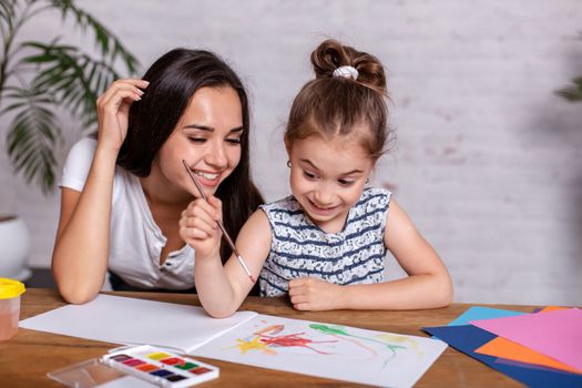 Happy family. Mother and daughter together paint. Woman helps the child girl.