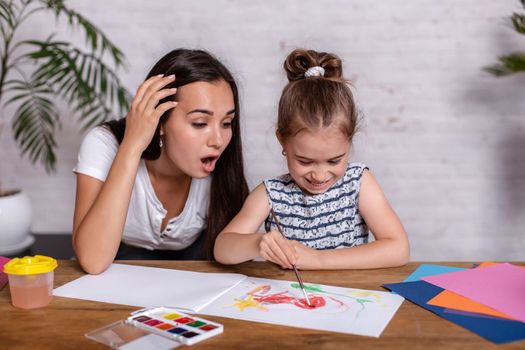 Happy family. Mother and daughter together paint. Woman helps the child girl.