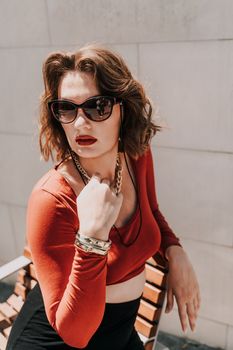 Portrait of a woman on the street. An attractive woman in glasses, a red blouse and a black skirt is sitting on a bench outside