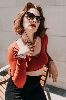 Portrait of a woman on the street. An attractive woman in glasses, a red blouse and a black skirt is sitting on a bench outside