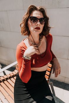 Portrait of a woman on the street. An attractive woman in glasses, a red blouse and a black skirt is sitting on a bench outside