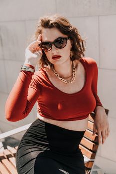 Portrait of a woman on the street. An attractive woman in glasses, a red blouse and a black skirt is sitting on a bench outside