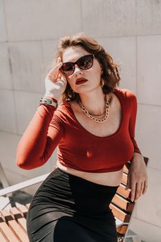 Portrait of a woman on the street. An attractive woman in glasses, a red blouse and a black skirt is sitting on a bench outside