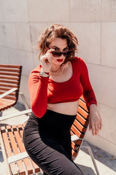 Portrait of a woman on the street. An attractive woman in glasses, a red blouse and a black skirt is sitting on a bench outside