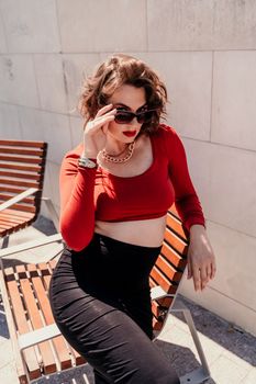 Portrait of a woman on the street. An attractive woman in glasses, a red blouse and a black skirt is sitting on a bench outside