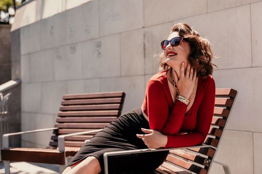 Portrait of a smiling woman on the street. An attractive woman with glasses, a red blouse and a black skirt is sitting on a bench on the street smiling