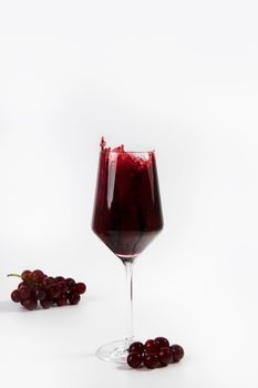 Wine glass with a splash of red wine and grapes isolated on white background copy space luxury