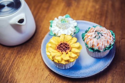 Various cupcakes decorated with colorful flower icing on wooden table, floral bouquet, wedding cake, High tea, Holiday concept Mothers day