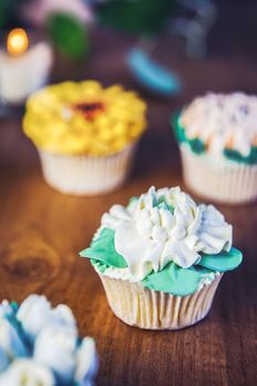 Various cupcakes decorated with colorful flower icing on wooden table, floral bouquet, wedding cake, High tea, Holiday concept Mothers day