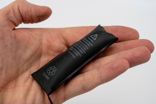 A swollen faulty smartphone battery in the hand of a smartphone repairman. Damages and malfunctions of mobile phones. Smartphone repair. Replacing the battery in a mobile phone