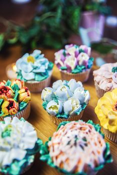 Various cupcakes decorated with colorful flower icing on wooden table, floral bouquet, wedding cake, High tea, Holiday concept Mothers day
