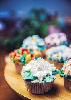 Various cupcakes decorated with colorful flower icing on wooden table, floral bouquet, wedding cake, High tea, Holiday concept Mothers day