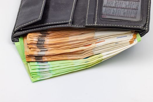 A black purse is overflowing with euro banknotes and cash as symbol of wealth