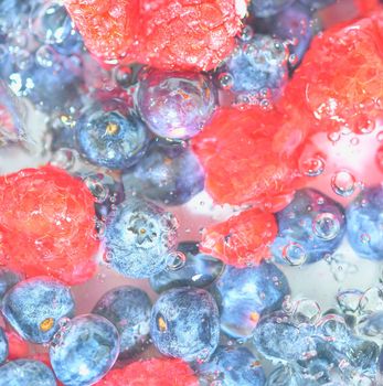Water with fresh berries, close-up. Close-up view of the blueberries and raspberries in water background. Texture of bilberries and raspberries with macro bubbles on the glass wall. Flat design, top view. Horizontal image. Defocused.