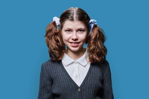 Portrait of a smiling child schoolgirl on a blue studio background. Preteen girl looking at the camera, wearing school clothes. School, kids, study education, childhood concept