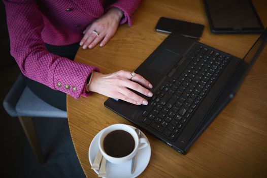 Top view of a businesswoman's hand on laptop keyboard while telecommuting from a cafeteria interior. Business on the go concept. Urban life. People. Lifestyle concept
