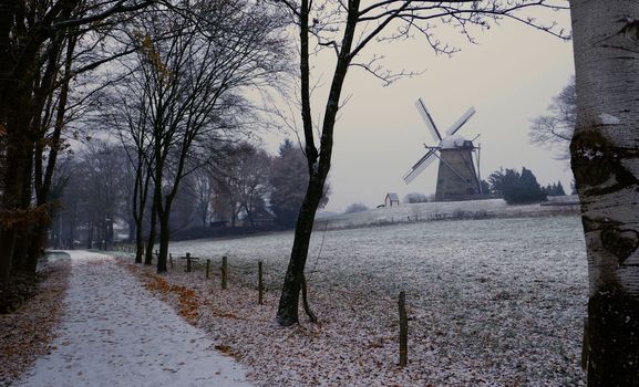 Idyllic image of a snow covered hiking trail. In the distance is an old windmill. Location: Uelsen, Germany