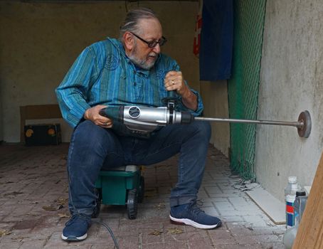 Active elderly man is drilling a hole in the wall of a garage with a jackhammer and a Rotary Hammer Core Bit