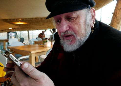 A man of almost seventy wearily checks his smartphone