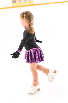 Little girl practicing figure skating on indoor ice skating rink.