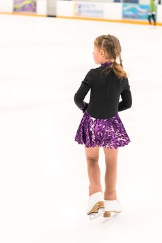 Little girl practicing figure skating on indoor ice skating rink.