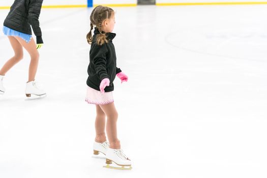 Little girl practicing figure skating on an indoor ice skating rink.