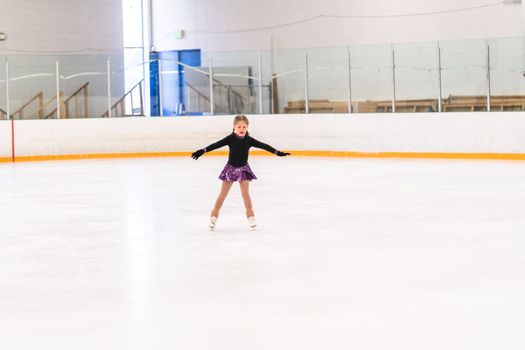 Little girl practicing figure skating on indoor ice skating rink.