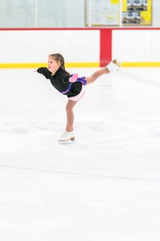 Little girl practicing figure skating on an indoor ice skating rink.