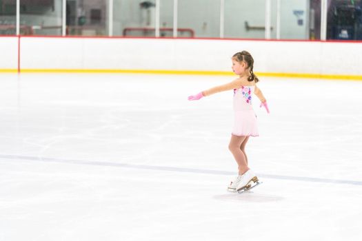 Little girl practicing figure skating on an indoor ice skating rink.