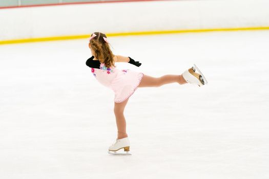 Little girl practicing figure skating on an indoor ice skating rink.