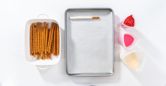 Flat lay. Dipping pretzels rods into silicone cup with melted chocolate to make chocolate-covered pretzel rods for Valentine's Day.