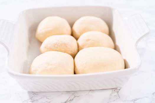 Rising dough in a white ceramic dish to prepare dinner rolls.