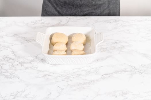 Rising dough in a white ceramic dish to prepare dinner rolls.
