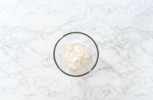Flat lay. Mixing dry ingredients with a hand whisk in a large glass mixing bowl to bake mini vanilla cupcakes with ombre pink buttercream frosting.