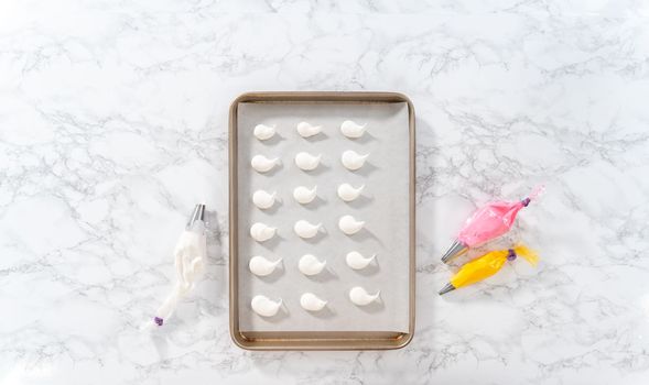 Piping meringue with piping bags into the baking sheet lined with parchment paper to bake Easter meringue cookies.