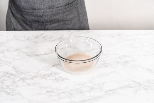 Activating dry yeast in a glass mixing bowl to prepare dinner rolls.