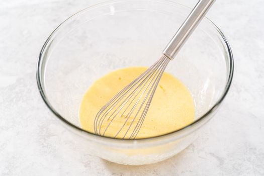 Mixing ingredients in a glass mixing bowl with a blending whisk to bake chocolate strawberry cupcakes.