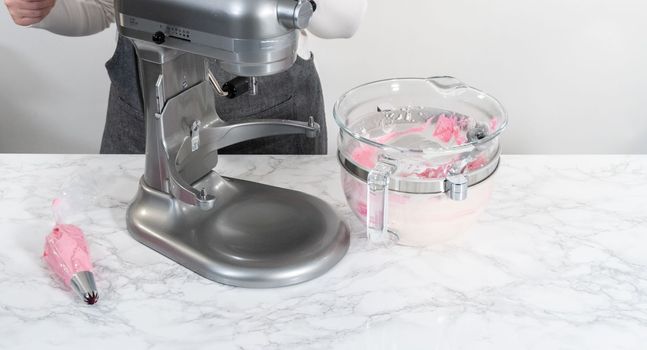 Mixing ingredients in kitchen electric mixer to make ombre pink buttercream frosting.