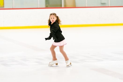 Little girl practicing figure skating on an indoor ice skating rink.