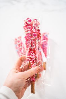 Chocolate-covered pretzel rods decorated with heart-shaped sprinkles for Valentine's Day packaged in a clear bags.