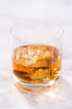 Scotch on the rocks in whiskey glass on a white marble surface.