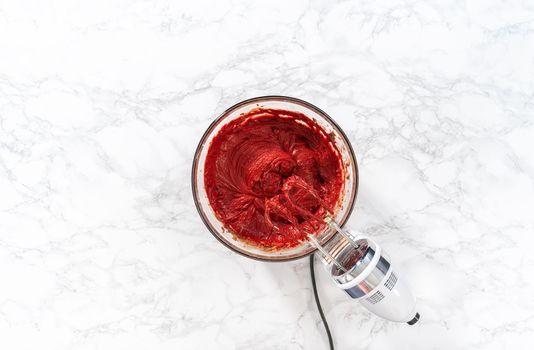 Flat lay. Mixing wet ingredients in a large glass mixing bowl to bake red velvet cupcakes with white chocolate ganache frosting.