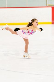 Little girl practicing figure skating on an indoor ice skating rink.