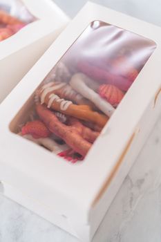 Packaging gourmet chocolate-covered pretzel twists into a white paper gift box filled with paper shreds.
