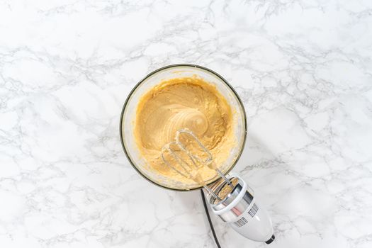 Flat lay. Mixing ingredients with a hand mixer in a large mixing bowl to bake eggnog bundt cake.