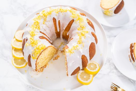 Sliced lemon bundt cake decorated with lemon zest on a cake stand.