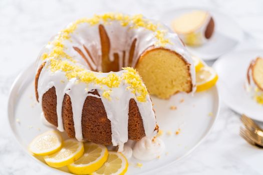 Sliced lemon bundt cake decorated with lemon zest on a cake stand.