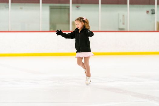 Little girl practicing figure skating on an indoor ice skating rink.