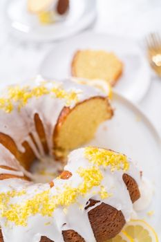Sliced lemon bundt cake decorated with lemon zest on a cake stand.